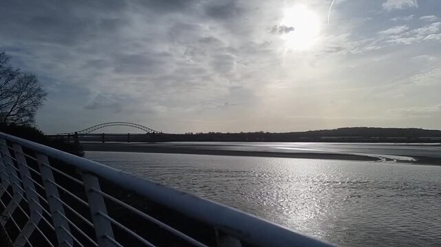 Panning across River Mersey shimmering estuary at sunrise under the Runcorn arched bridge crossing