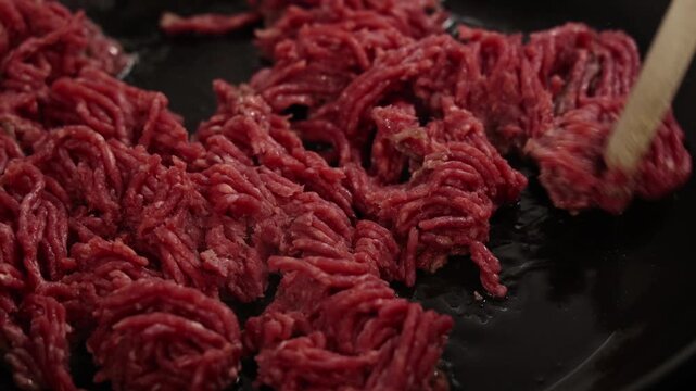 Raw minced meat being stirred in pan during cooking preparation in kitchen.