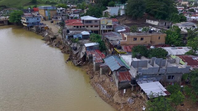 Aerial view of river flooding and erosion damaging homes in Gaspar Hernandez, Dominican Republic, after heavy rains, showing collapsed riverbanks, vulnerable housing and natural disaster impact.