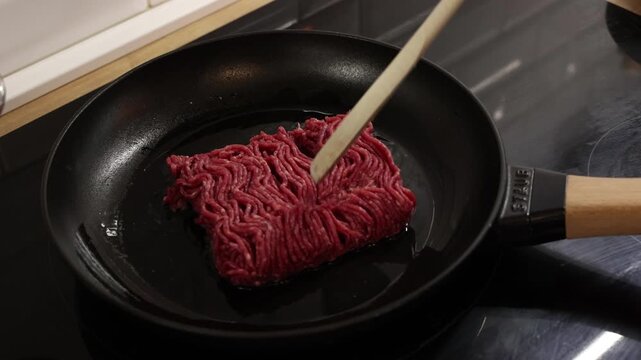 Raw ground beef placed into frying pan on stovetop ready to start cooking process.