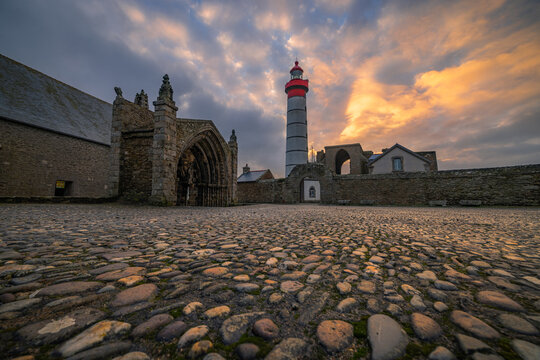 View of the Saint-Mathieu Lighthouse and the ruins of the ancient abbey over a cobblestone path at sunset in Plougonvelin, Brittany, France.