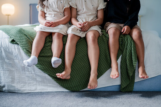 Three young kids sitting closely with small legs dangling freely on the bed