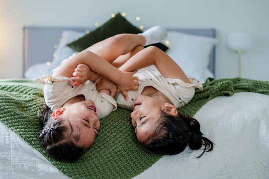 Two young girls having fun wrestling on a bed covered with a green blanket