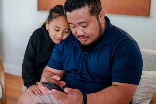 Samoan man scrolling through his phone while son looks over his shoulder