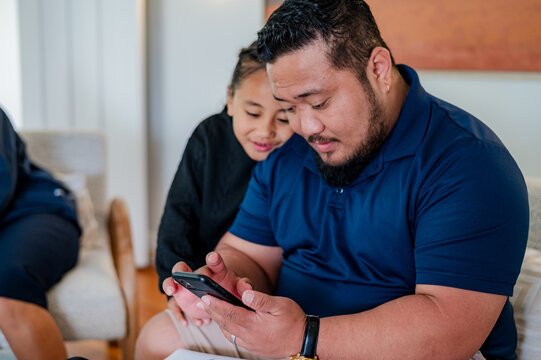 Samoan man scrolling through his phone while son looks over his shoulder