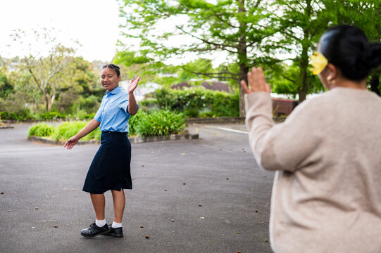 Teenage girl in school uniform waving at mum in school driveway