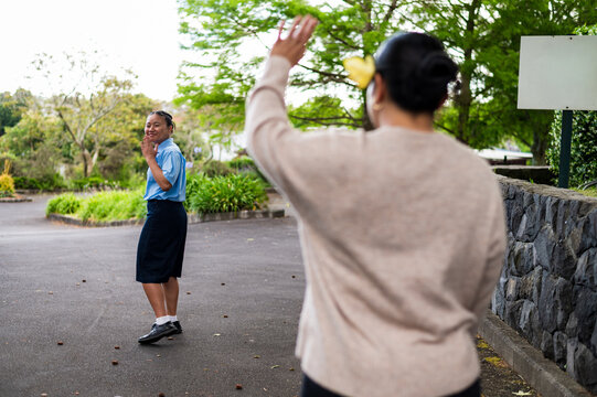 Teenage girl in school uniform waving at mum in school driveway
