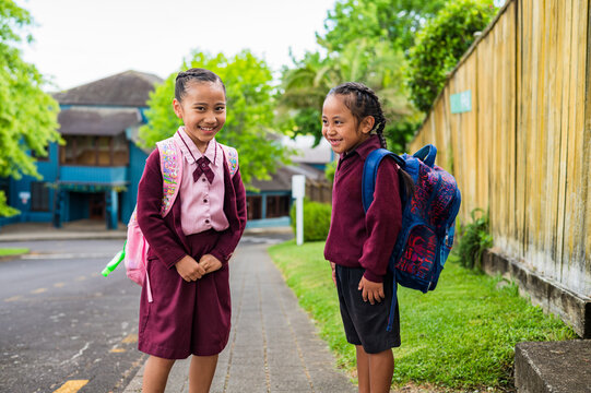 Two young school kids carrying backpacks standing on the sidewalk laughing