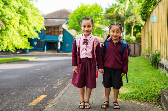 Two school kids in uniform standing on the sidewalk holding hands
