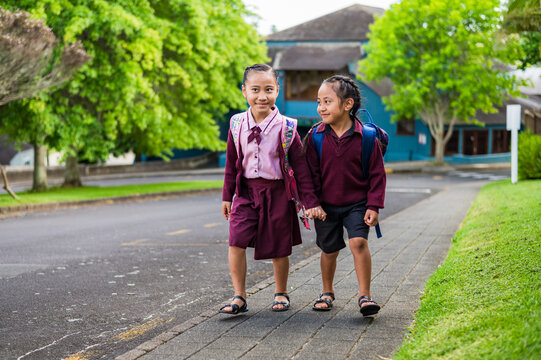 Two young kids in school uniform walking on the sidewalk holding hands