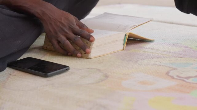 Black student hands on book phone, fingers tracing lines on pages, colorful patterned rug beneath, focused revision vibe, modern device at side, quiet indoor concentration, mindful study moment