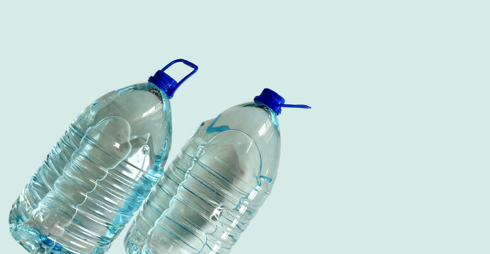 Drinking water bottles, light blue background. Transparent 5l bottles, full, blue cap, with handle. Clean water supply concept.