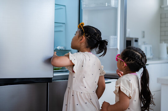 Two young girls wearing flower sunglasses opening the fridge looking for a snack