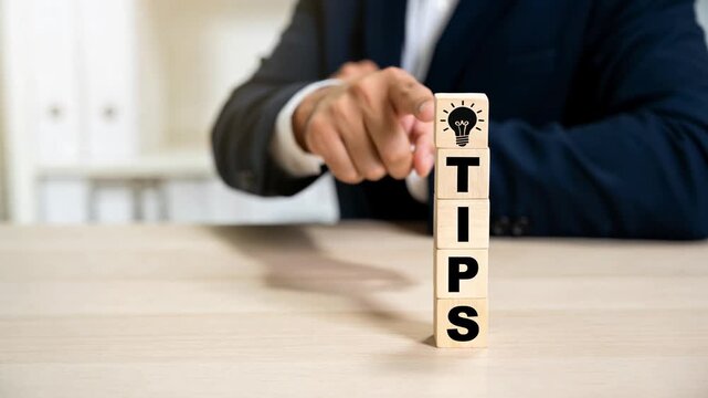 Businessman's hand placing idea icon on wooden blocks spelling TIPS for advice and strategy concept with copy space.