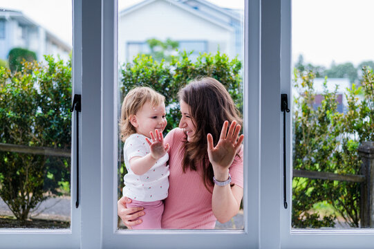 Italian mum carrying toddler daughter outdoors pressing their hands against glass window