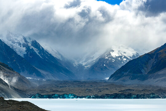Face of a glacier across a lake with snow covered alpine mountains in the background