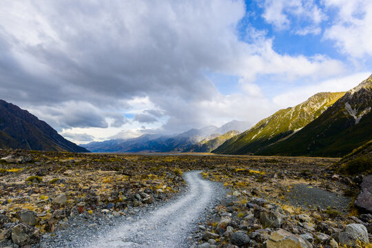 View along gravel track to snow capped mountains with a cloudy sky