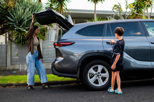 Young boy opening the rear passenger door of the car while mum closes the boot