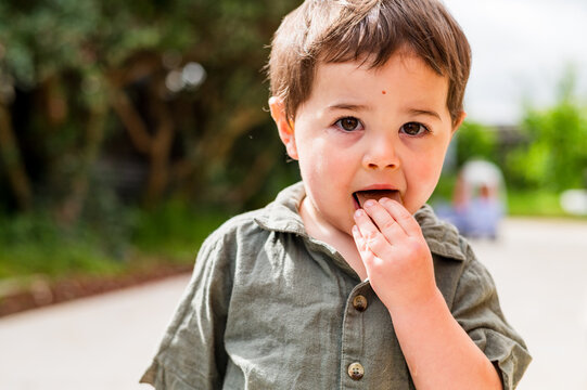 Close up of toddler boy putting his hand in his mouth while standing in the backyard