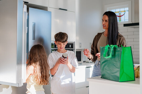 Mother and children standing by a fridge while son is checking the label of one bottle