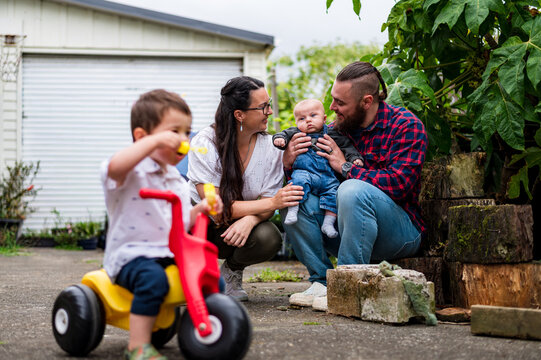 Toddler boy on his trike toy blowing bubbles in the backyard with parent in the background
