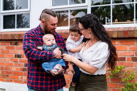 Happy couple standing in front of the brick walls holding an infant and toddler son