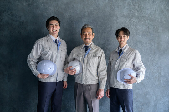 グレー背景で並んで笑顔の作業服を着た日本人男性
