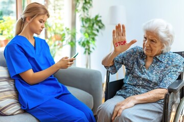 Obraz premium Senior Woman Shows STOP to Neglectful Nurse Focused on Her Smartphone