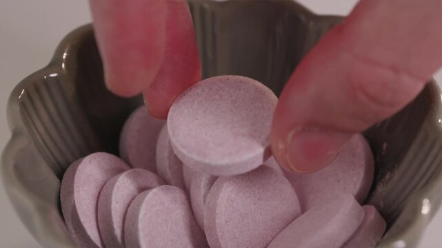 Horizontal macro shot of a hand selecting a red effervescent tablet. Clean, bright background emphasizing the pharmaceutical quality and minimalist aesthetic.