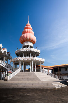 View of the Arya Dewaker Hindu Temple featuring its unique white tiered architecture and pink dome under a clear blue sky in Paramaribo, Paramaribo District, Suriname.