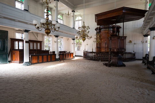 View of the interior of the Neveh Shalom Synagogue featuring its unique sand floor, wooden pulpit, and ornate brass chandeliers in Paramaribo, Paramaribo District, Suriname.
