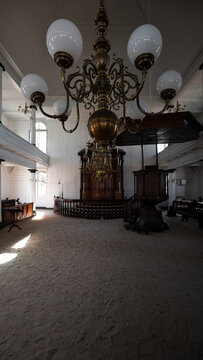 View of the Neveh Shalom Synagogue interior featuring a unique sand floor, ornate brass chandeliers, and dark wood furnishings in Paramaribo, Paramaribo District, Suriname.