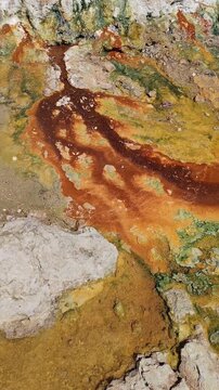 Natural thermal spring with rusty iron and white sulfur deposits flowing into the sea. Vibrant mineral patterns and geological textures at Loutra Edipsos, Evia island, Greece