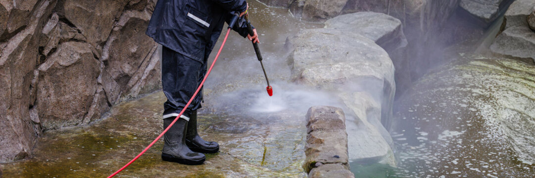Worker cleaning stone wall with pressure washer removing dirt and algae outdoor