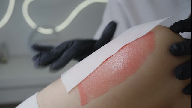 Applying warm wax on leg during professional epilation treatment