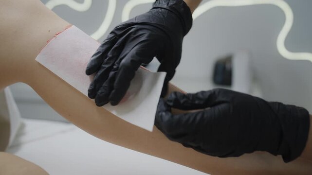 Removing wax strip from leg during professional epilation treatment