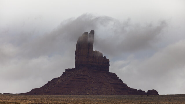 View of a sandstone butte shrouded in low clouds and mist under an overcast sky in Oljato-Monument Valley, Arizona, United States.