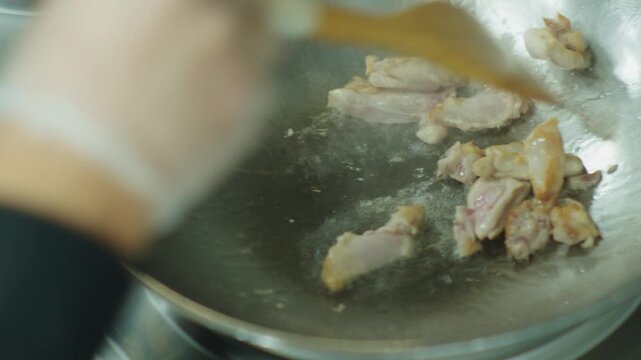 A chef fries chicken meat in a deep iron wok. Asian food in oil.