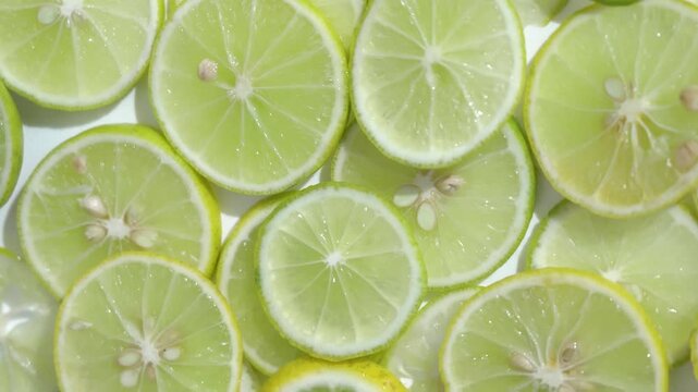 Top view of juicy green lime slices overlapping on white background, 4K footage