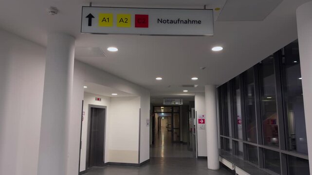Hallway of large German medical facility, featuring overhead sign directing patients to Notaufnahme (emergency reception). Dark evening. Empty and clean. Krankenhaus Deutschland. 