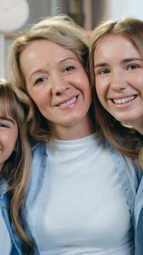 People feelings concept where attractive joyful loving caring mom and two different ages daughters sitting on the couch in front of camera with sincerely smiles in contemporary sitting room