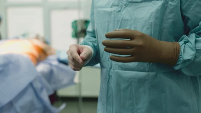 Close up unrecognizable surgeon man putting on surgery gloves male hands doctor with assistant put on uniform in hospital clinic two unknown doctors ready for operation healthcare medicine safety
