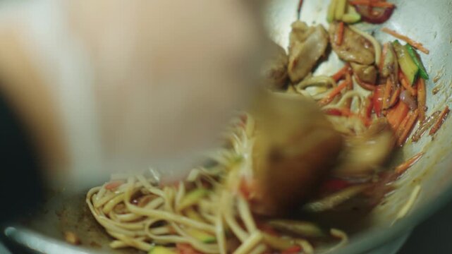 A cook stirs cooked noodles in a wok over a fire. Asian food. Cooking noodles. Stir-frying noodles with vegetables.
