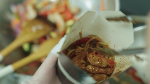 A cook places cooked Chinese noodles in a wok box. Asian food. Fast food. Hot noodles in a box.
