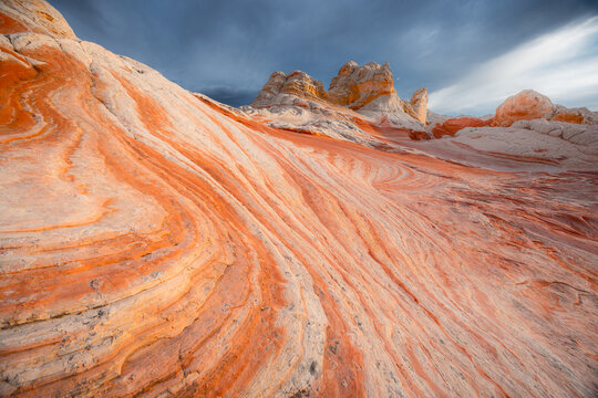 View of the unique swirling orange and white sandstone formations at White Pocket under a dramatic cloudy sky in Coconino County, Arizona, United States.