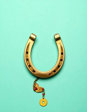 A golden horseshoe hangs centered against a pale green backdrop, adorned with a small chain, coins and red beads