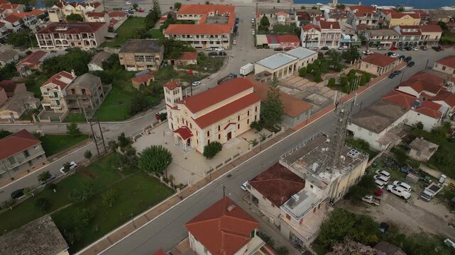 An aerial view of a small town features a prominent church, residential buildings with red roofs, and a few commercial structures.