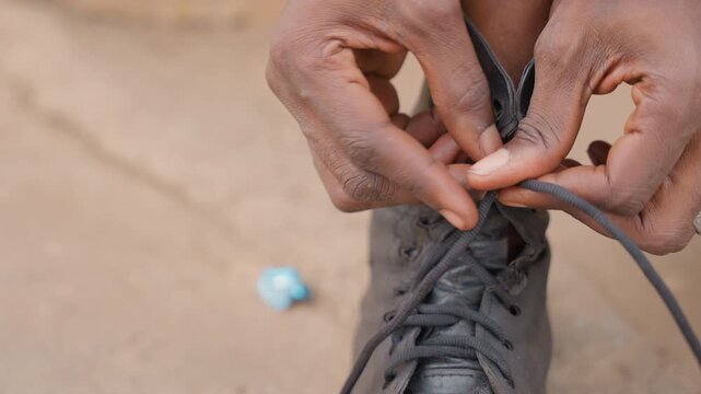 Black man tying boot laces on porch before house chores, closeup on practiced fingers and knot formation, steady rhythm and patient dexterity, final prep for daily labor and outdoor tasks