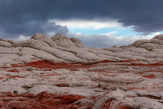 View of White Pocket rock formations with brain-like textures and red sandstone under a dramatic cloudy sky in Coconino County, Arizona, United States.
