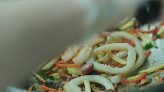A chef fries seafood with vegetables in a wok. Squid and octopus are fried in oil in a deep metal pan. Cooking seafood